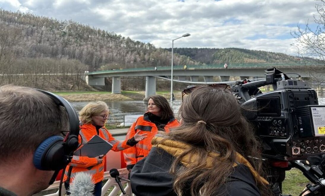Zwei Frauen in orangenen Jacken sprechen vor Journalisten mit Fernsehkameras