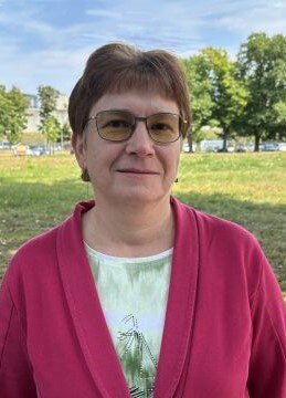 Frau mit Glitzer-T-Shirt und pinkfarbigem Blazer vor einer Wiese