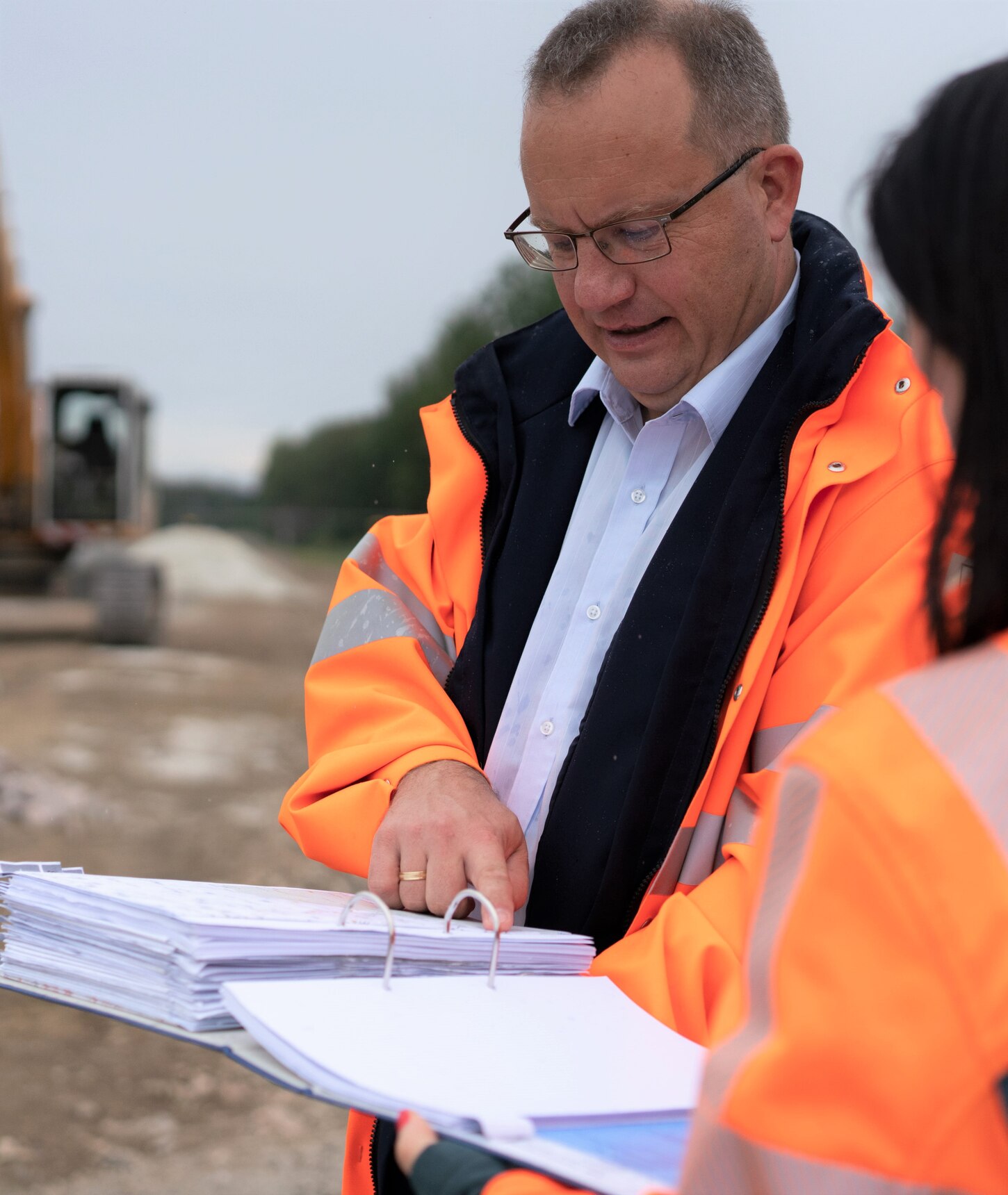 Zwei Kollegen in orangener Arbeitskleidung, die an einer Baustelle ein Besprechung zusammen haben