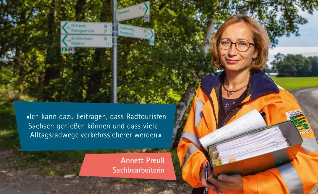 Frau mit Aktenordnern vor Wegweiser für Fahrradwege; Annett Preuß: Ich kann dazu beitragen, dass Radtouristen Sachsen genießen können und dass viele Alltagsradwege verkehrssicherer werden.