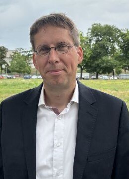 Ein Mann mit geöffnetem Hemd und einem schwarzen Anzug vor einer Wiese