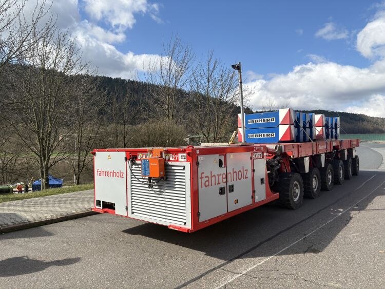 Ein rotes Schwerlastfahrzeug mit tonnenschweren Betonklötzen, das über eine Brücke fährt.